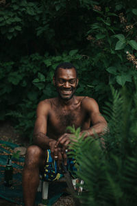 Portrait of shirtless man sitting by plants