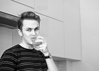 Portrait of smiling man drinking water from glass at home