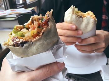 Cropped hands holding burritos at restaurant