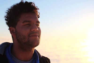 Close-up of young man looking away against sky during sunset