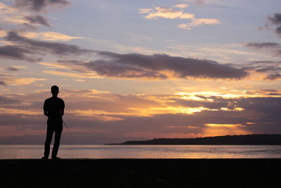 Silhouette man looking at sea against sky during sunset