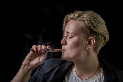 Close-up of young woman smoking over black background