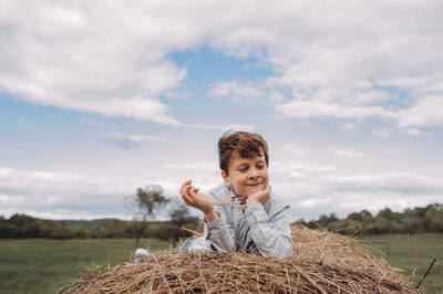 Portrait of boy with arms raised on field against sky