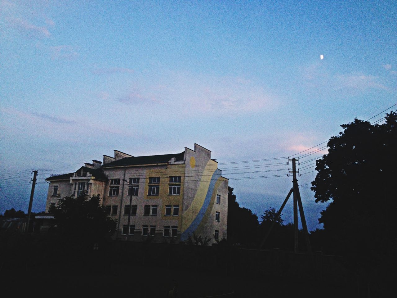 building exterior, architecture, built structure, sky, city, building, low angle view, residential building, transportation, cloud - sky, residential structure, silhouette, mode of transport, dusk, power line, outdoors, no people, day, crane - construction machinery, tree