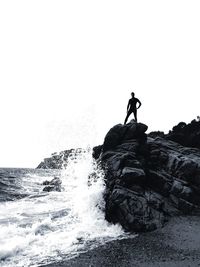 People on rock by sea against clear sky