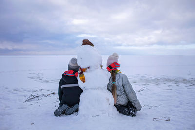 Boy and girl sit together with snowman and look forward. loneliness and snow friend. winter mood