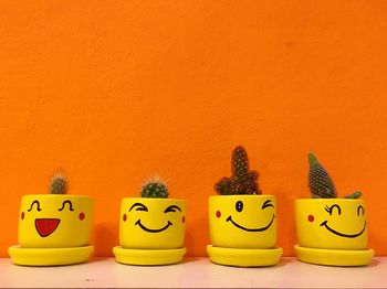 Yellow and potted plants on table against orange wall