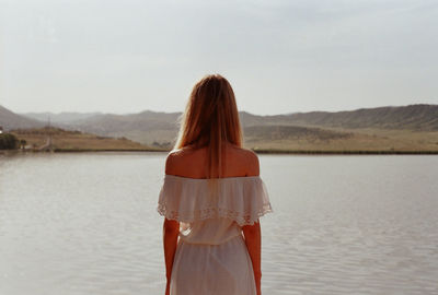 Rear view of young woman standing on lakeshore