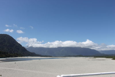 Scenic view of road by mountains against blue sky