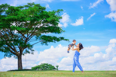 Woman standing by tree on field against sky