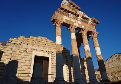 Low angle view of old roman temple in city against blue sky