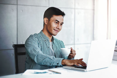 Young man using phone while sitting on table