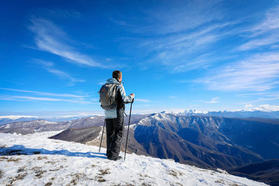 Rear view of man standing on snowcapped mountain against sky