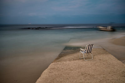 Empty chair on shore at beach against sky