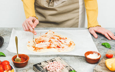 Hands of a caucasian teenage girl in an apron cut out the dough in the shape of a heart for pizza.