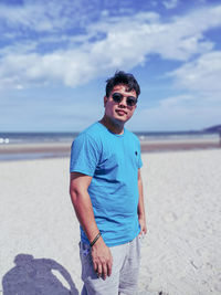 Portrait of young man standing at beach against sky