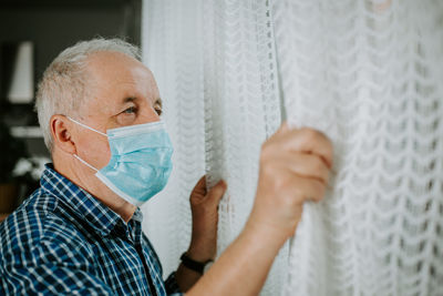 Close-up man wearing mask holding curtain