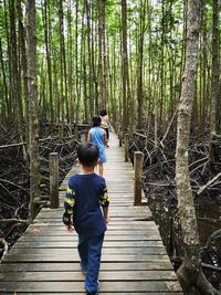 Rear view of mother with kids walking on pier in forest