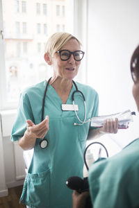 Smiling mature pediatrician gesturing while talking to female healthcare worker in clinic