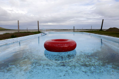 Red inflatable ring in swimming pool against sky