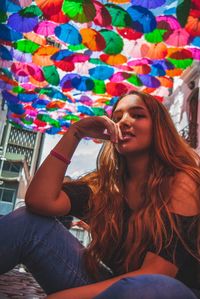 Portrait of young woman sitting against multi colored umbrellas