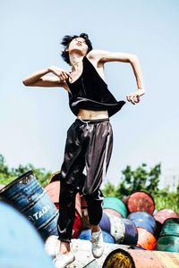 Full length of young woman jumping against oil drums