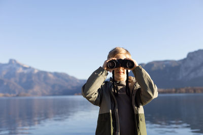 Boy looking through binocular against sky