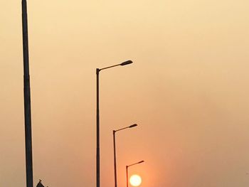 Low angle view of street lights against orange sky
