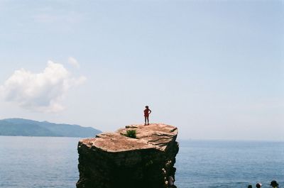 Man standing on rock by sea against sky