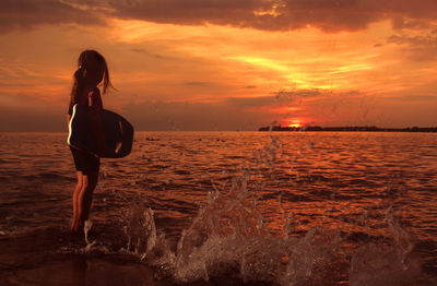 Girl standing in sea against sky during sunset