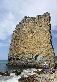 People on rock by sea against sky