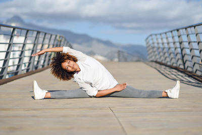 Woman stretching legs on boardwalk against sky