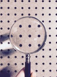Cropped hand holding magnifying glass in front of patterned wall