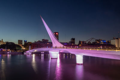 Illuminated bridge over river against clear sky at night