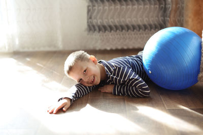 Boy near the fitness ball, tired and joyful resting on the floor, a real interior, a sunny day