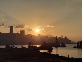 Silhouette cityscape by sea against sky during sunset