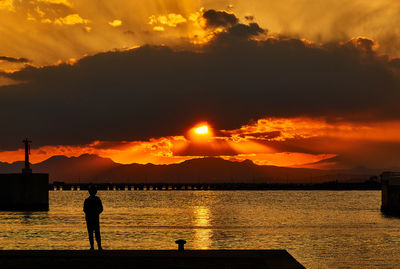 Silhouette people standing by sea against sky during sunset