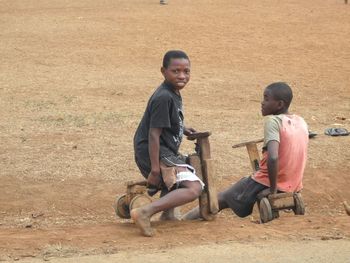 Portrait of boy riding wooden tricycle with friend on field