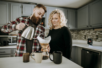 Man pours hot water into coffee pour over while wife looks on