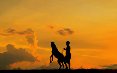 Silhouette man with horse on field against orange sky during sunset