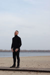 Portrait of young man standing on beach against sky