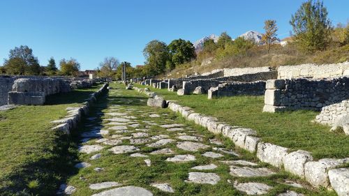 Grassy pathway amidst stone walls against clear sky