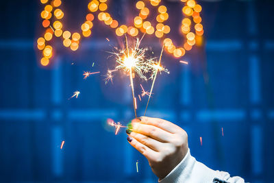 Cropped hand of woman holding illuminated sparklers at night
