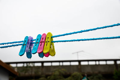 Close-up of clothespins hanging on rope against sky