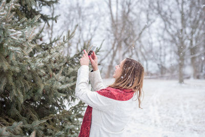 Woman photographing christmas tree during snowfall