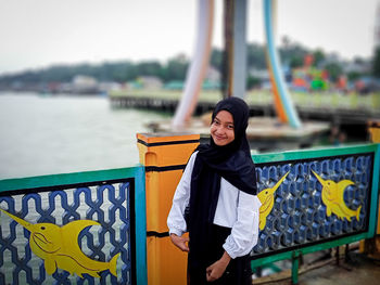 Portrait of smiling young woman standing against railing