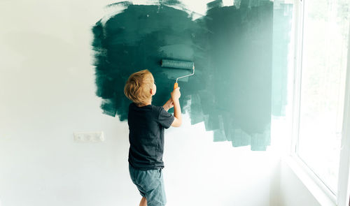 Side view of boy painting on wall at home