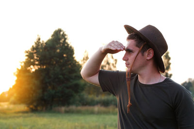 Young man farmer in cowboy hat at agricultural field on sunset with sun flare. closeup portrait 