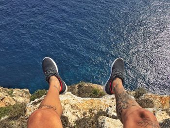 Low section of tattooed man sitting over sea during sunny day