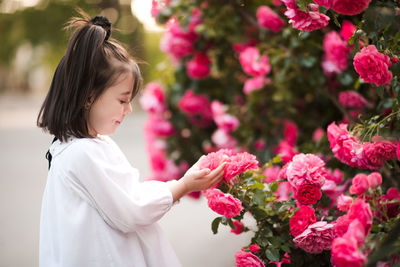 Beautiful baby girl 3-4 year old holding fresh pink roses in garden outdoors closeup. summer season.
